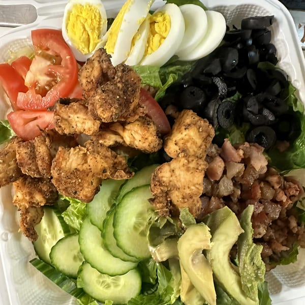 A vibrant salad with Cajun chicken, sliced tomatoes, hard-boiled eggs, olives, cucumbers, and avocado.