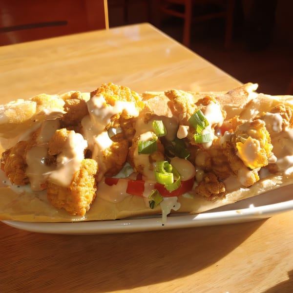 A close-up of a Cajun shrimp po'boy sandwich with sauce, tomatoes, and green onions.