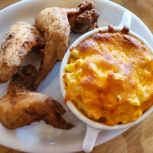 Cajun fried chicken wings and a side of baked macaroni and cheese in a white bowl.