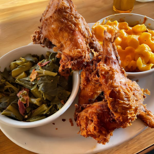 Cajun fried chicken with sides of collard greens and macaroni and cheese on a white plate.