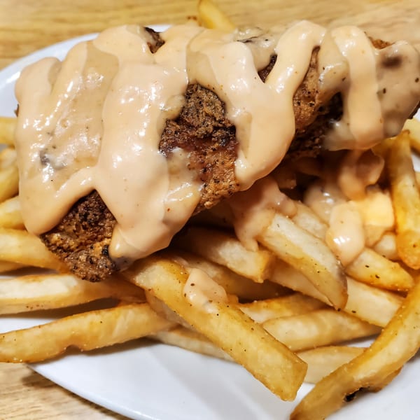Cajun fried chicken and french fries covered in a creamy sauce on a white plate.
