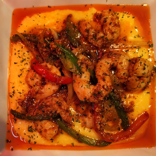 Cajun shrimp and grits with bell peppers and onions in a white bowl.