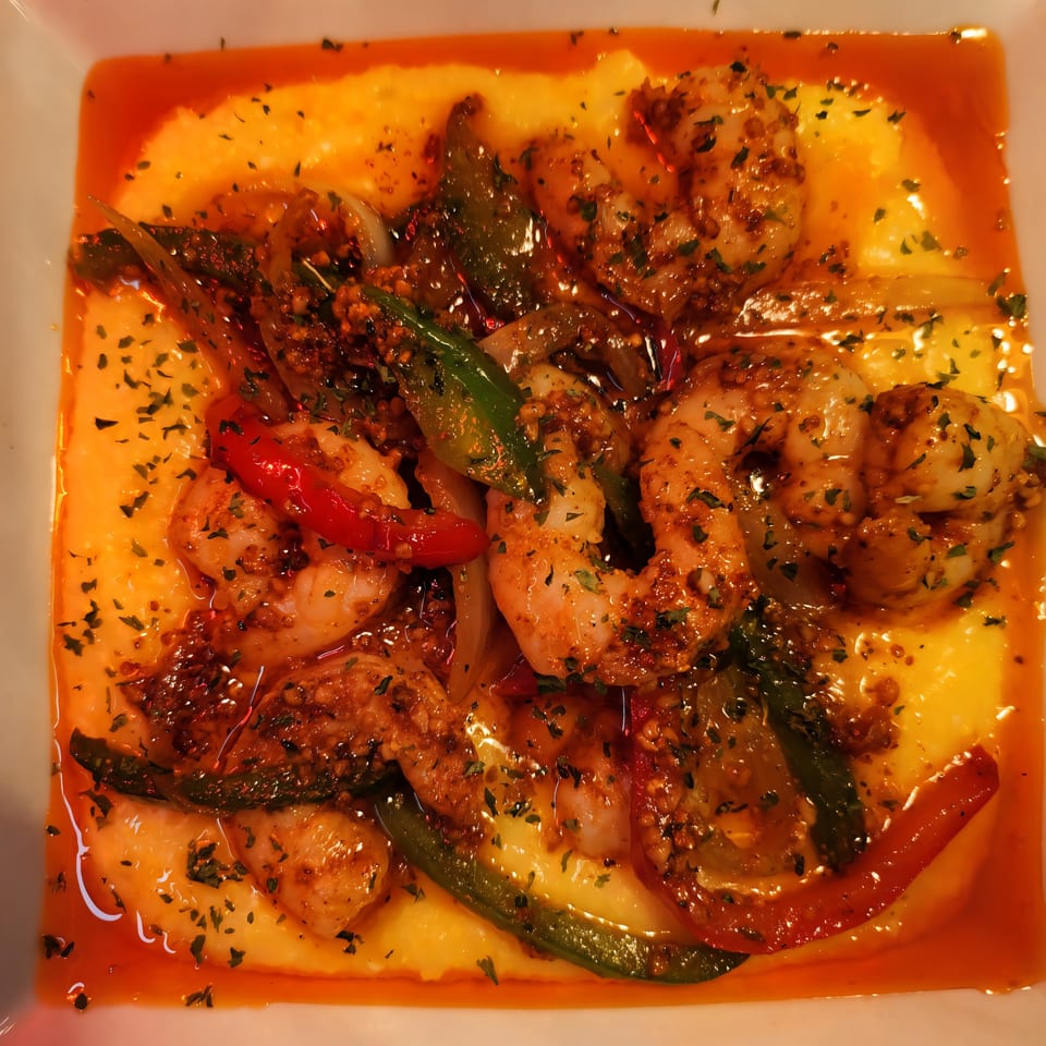 Cajun shrimp and grits with bell peppers and onions in a white bowl.