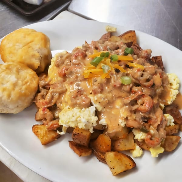 Cajun breakfast with scrambled eggs, shrimp and gravy, home fries, and two biscuits on a white plate.